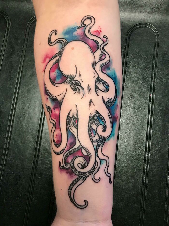 Watercolor tattoo of an octopus with vibrant blue and pink accents on an arm.