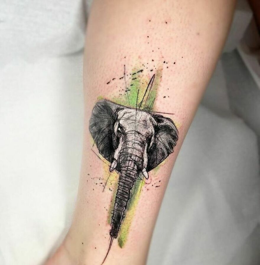 Watercolor tattoo of an elephant head on forearm, featuring green accents and abstract details.