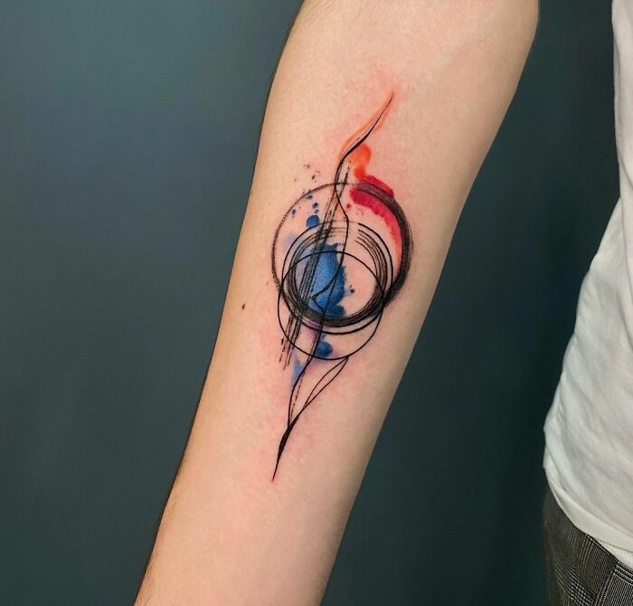 Abstract watercolor tattoo on forearm with colorful ink splashes and swirling black lines.