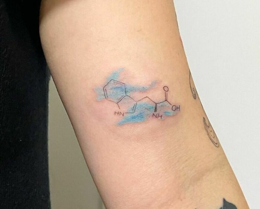 Watercolor tattoo with a chemical structure on the arm, featuring blue shading.