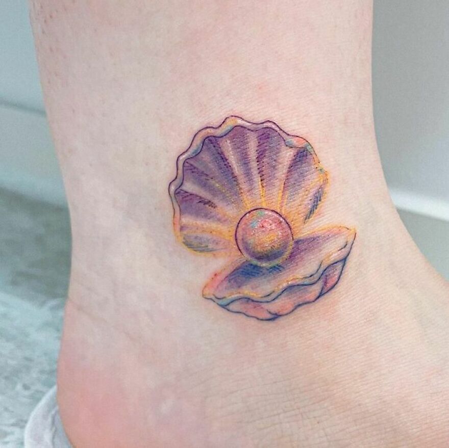 Watercolor tattoo of an open seashell with a pearl on an ankle.