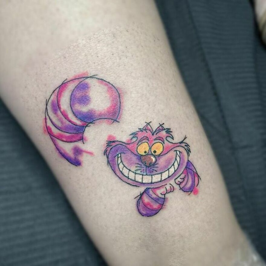 Colorful watercolor tattoo of a smiling cartoon cat on a person's skin.