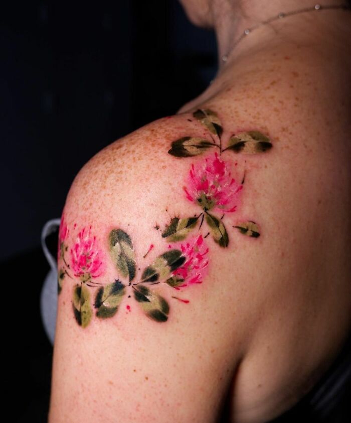 Watercolor tattoo of pink flowers and green leaves on a shoulder, showcasing inkspiration.