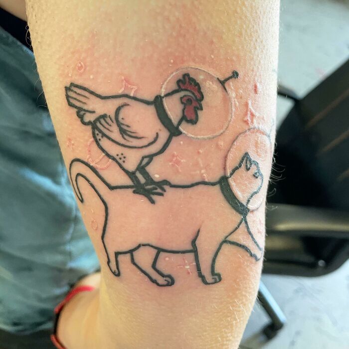 Tattoo of a chicken and a cat with helmets, showcasing adorable pet-themed body art.