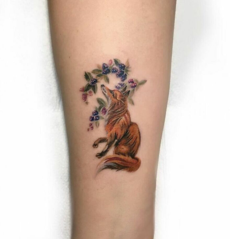 Watercolor tattoo of a fox surrounded by colorful flowers on forearm.