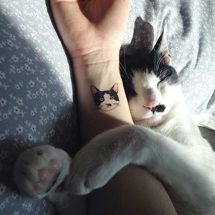 Cat tattoo on wrist with sleeping black and white cat, showcasing adorable pet tattoos.