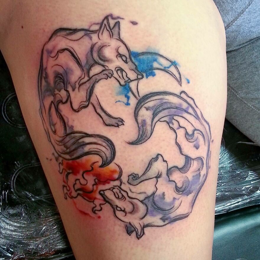 Watercolor tattoo of two stylized foxes with blue and red accents on skin.