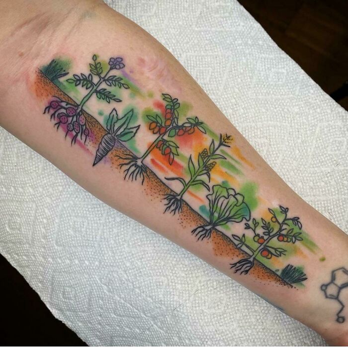 Watercolor tattoo of colorful vegetables and roots on a forearm, showcasing ethereal garden artistry.