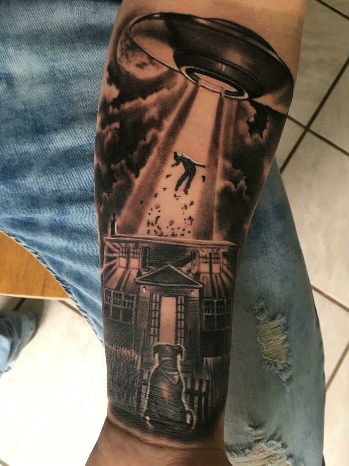 Pet tattoo of a UFO abducting a dog in front of a house, illustrating creative and adorable ways to immortalize pets.