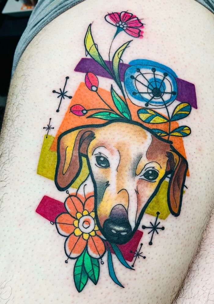 Tattoo of a dog's face with colorful flowers and abstract shapes, celebrating furry friends.