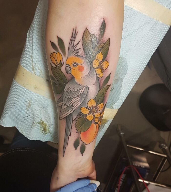 Pet tattoo of a cockatiel with colorful flowers on a person's arm, symbolizing the bond between humans and pets.