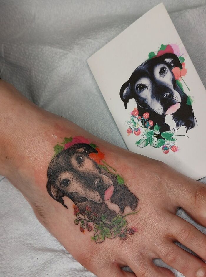 Pet tattoo of a dog on a person's foot, matching a colorful design on paper nearby.