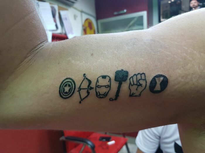 Marvel tattoos featuring iconic symbols on a person's arm, showcasing superhero themes in bold black ink.