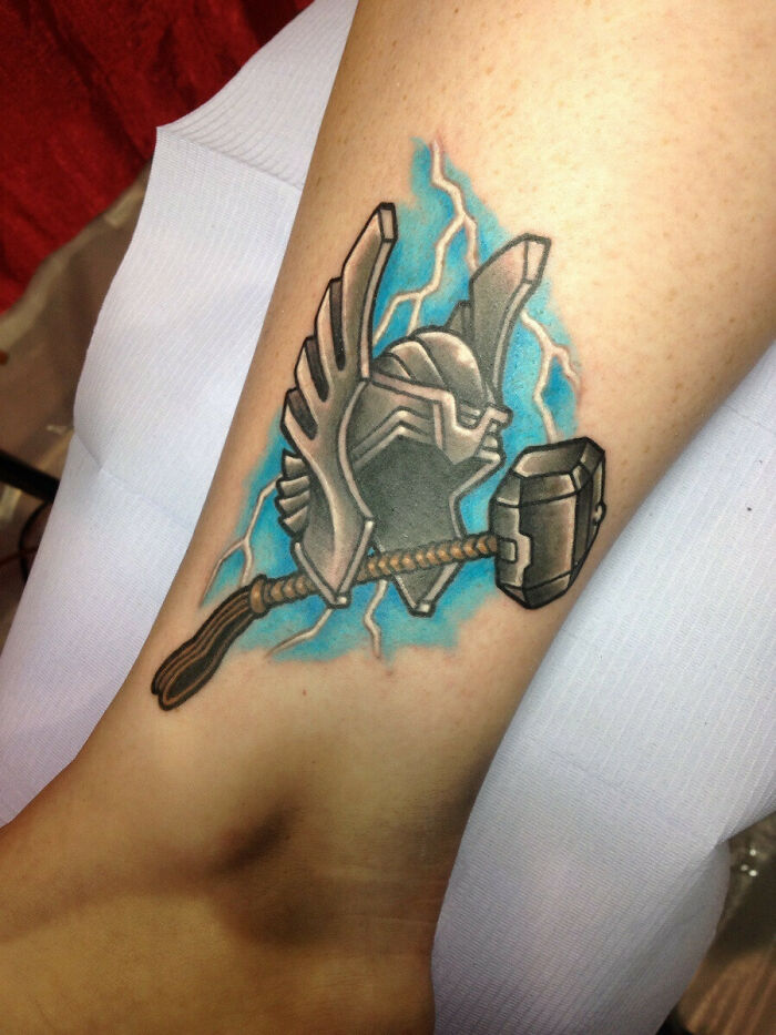 Thor helmet and hammer Marvel tattoo with lightning on forearm.