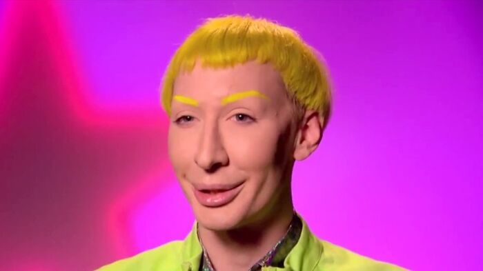 Person with a unique haircut and bright yellow hair against a pink background.