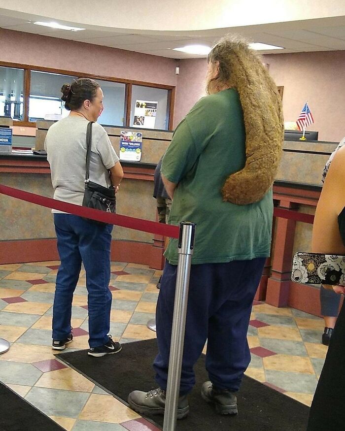 Man with an unusual, long dreadlock hairstyle standing in line at a bank next to a woman.