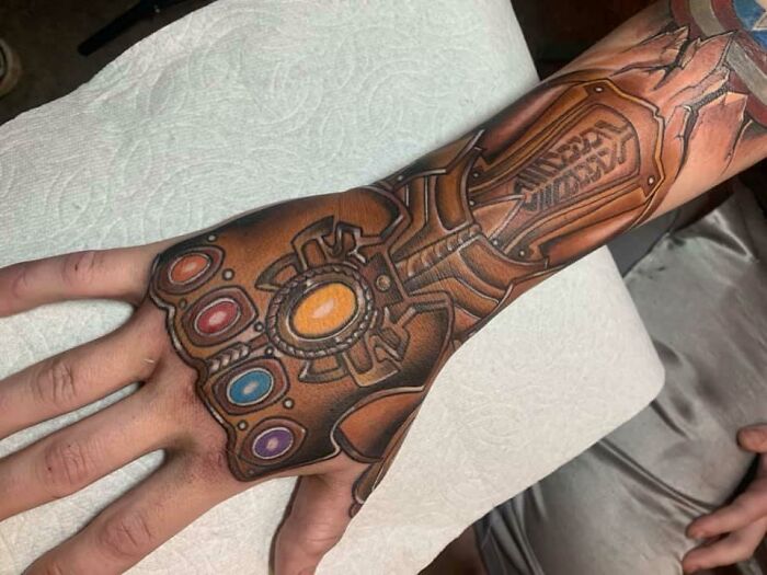 Marvel tattoo of the Infinity Gauntlet with colorful stones on an arm, showcasing intricate design and detail.
