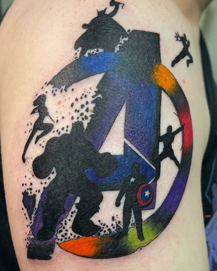 Marvel tattoo featuring superhero silhouettes in a colorful Avengers emblem.