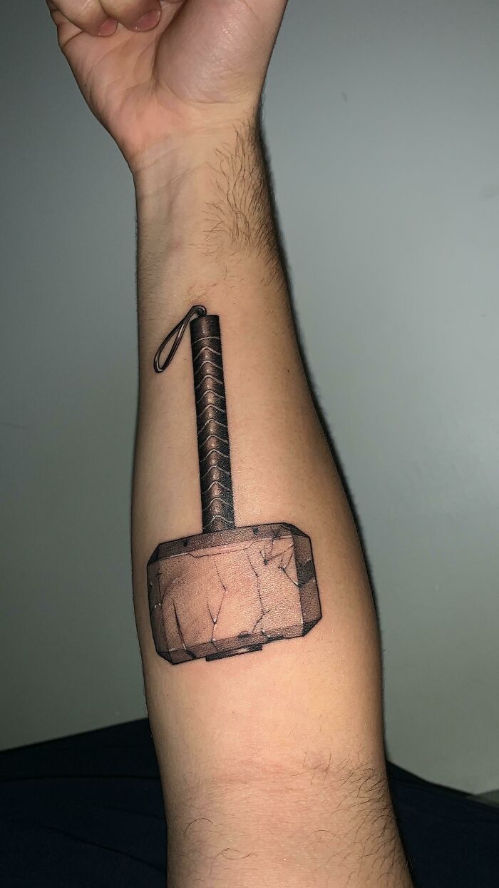 Arm with detailed Marvel tattoo of Thor's hammer, showcasing superhero artwork.