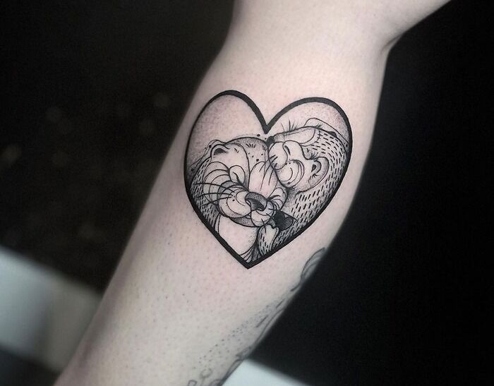 Animal tattoo of two otters in a heart design on someone's forearm.