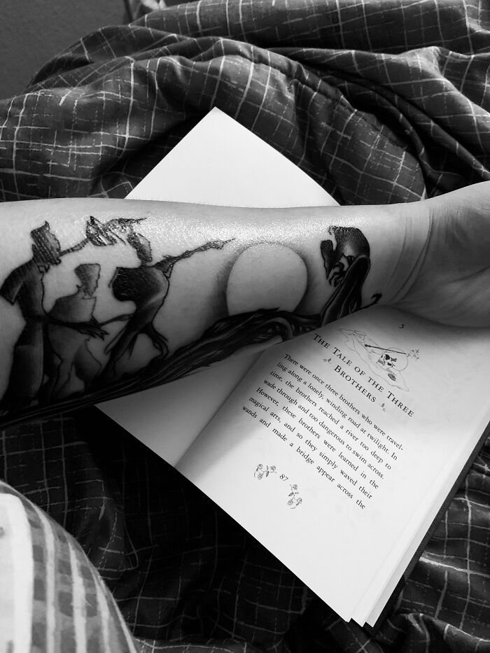 Arm tattoo of "The Tale of the Three Brothers" from Harry Potter next to an open book.