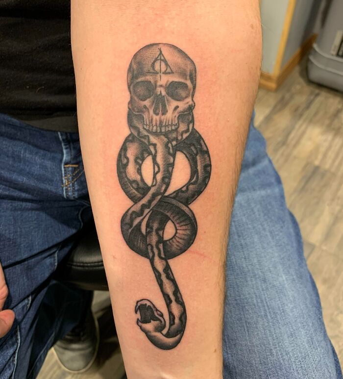 Harry Potter tattoo of a skull with a snake on an arm, featuring the Deathly Hallows symbol.