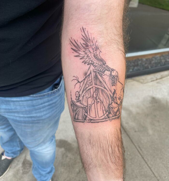 Arm with a detailed Harry Potter tattoo, featuring a winged creature and mystical symbols.