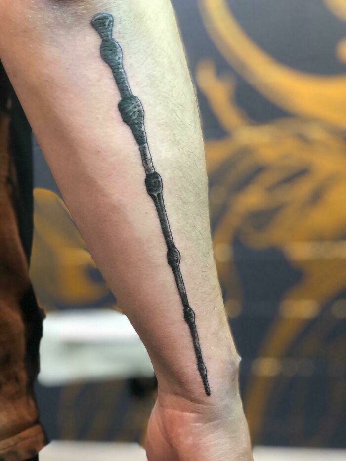 Arm with Harry Potter wand tattoo, featuring intricate black ink design.