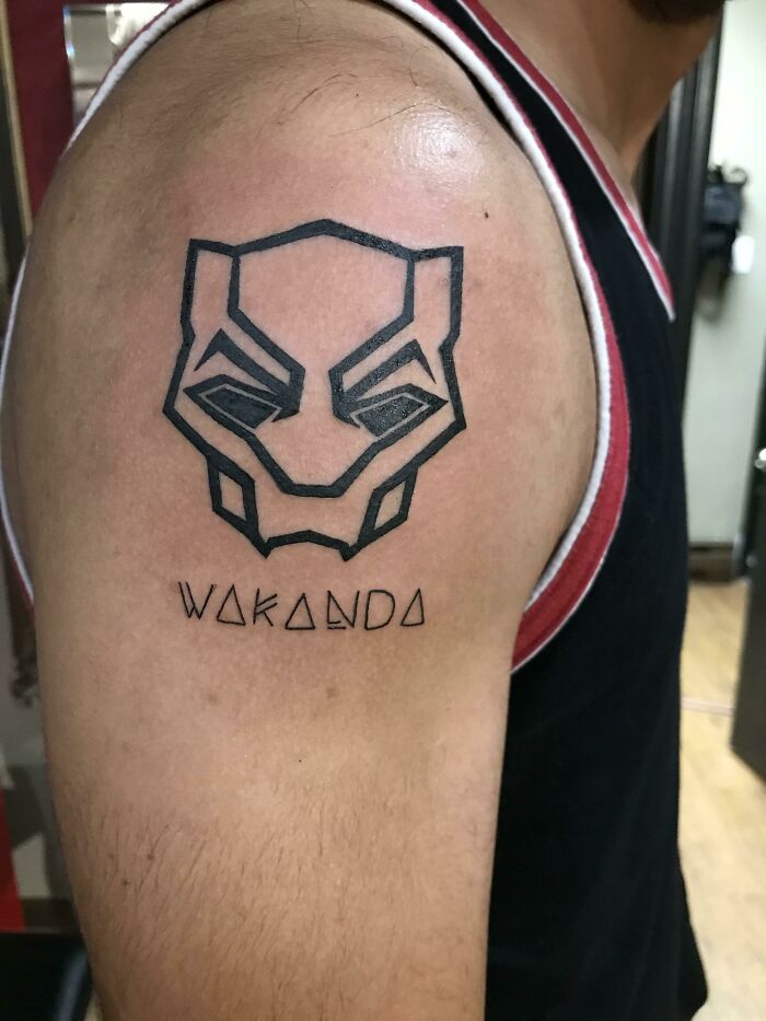 Marvel tattoo of Black Panther mask and "Wakanda" text on upper arm.