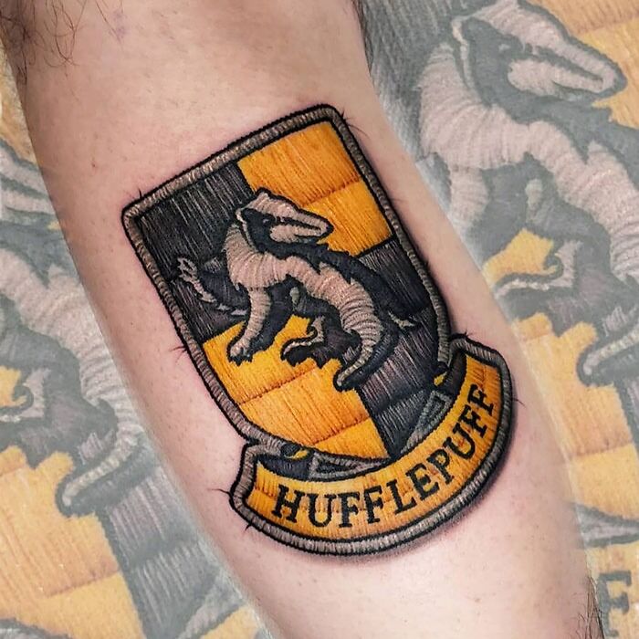 Hufflepuff badge tattoo on forearm, featuring a badger emblem in yellow and black stripes.