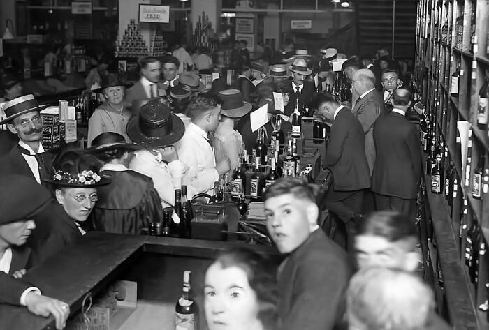 Crowded vintage bar scene with men and women in early 20th century attire, highlighting big historical events around a century ago.