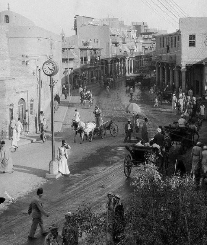 Black and white photo of a busy street with horse-drawn carriages capturing big historical events around a century ago.