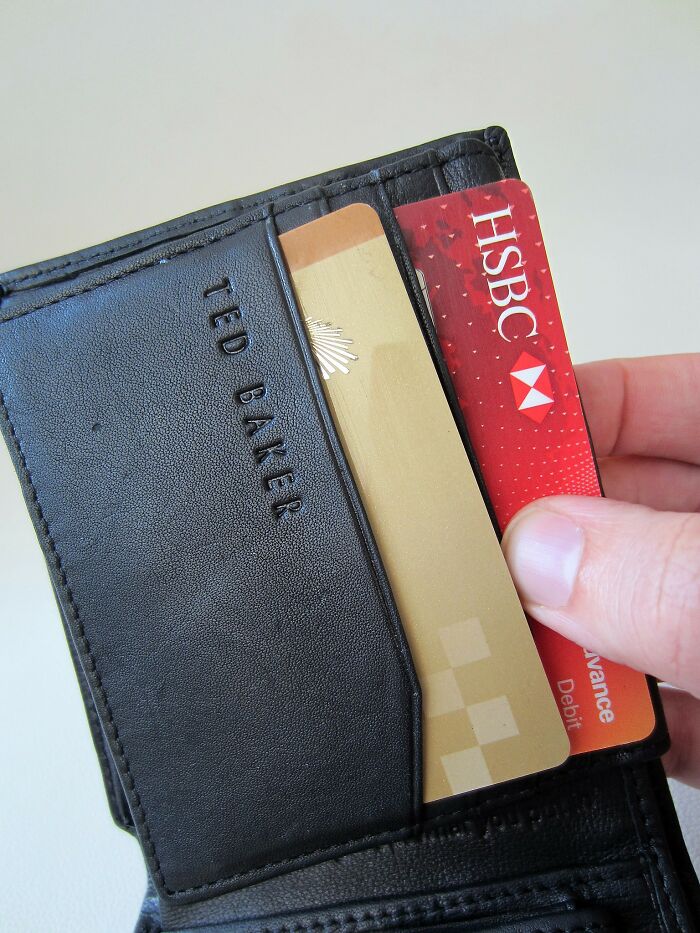 Hand holding a Ted Baker wallet with credit and debit cards, illustrating things you may not think of doing but would be committing a crime.