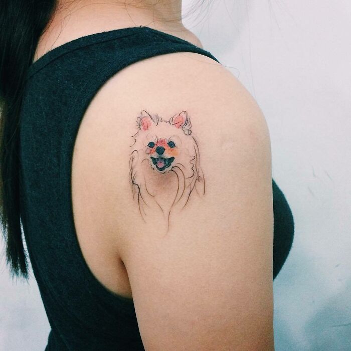 Pet tattoo of a small dog on a woman's shoulder, celebrating furry friends with a minimalist design.