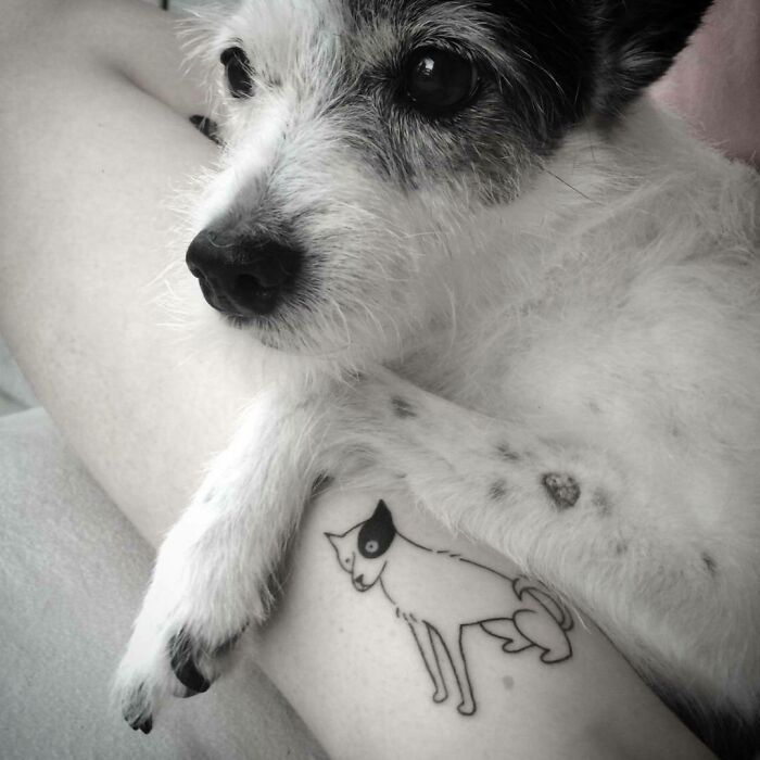 Adorable pet tattoo on arm with matching dog lying nearby, showcasing pet love.