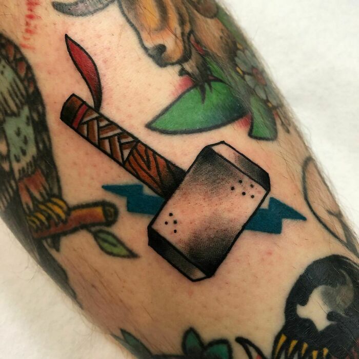 Marvel tattoo of Thor's hammer, Mjolnir, with colorful background elements on arm.
