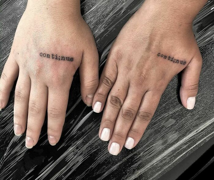 "Word tattoo on hands displaying 'continue' in black ink."