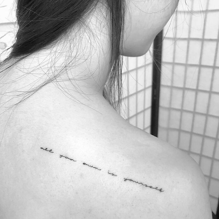 Minimalist word tattoo on shoulder in elegant script, conveying a personal message for creative inkspiration.