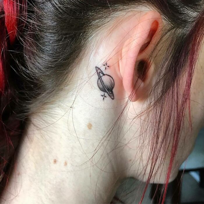 Minimalist planet ear tattoo with stars, showcasing subtle tattoo design.