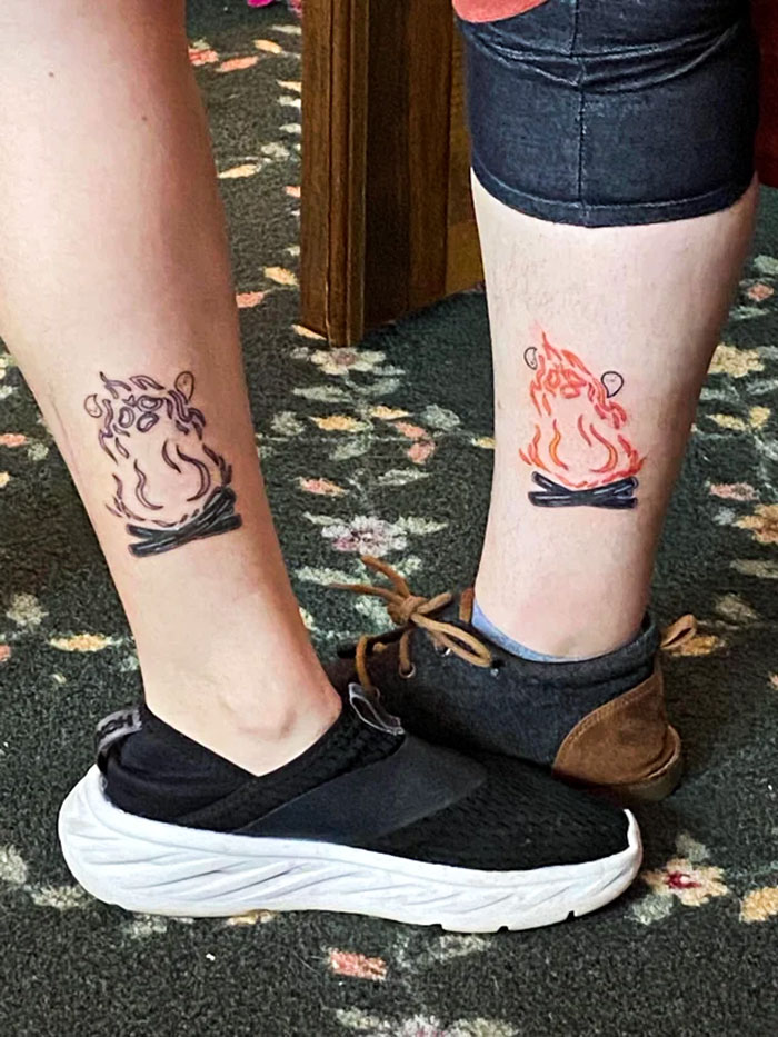 Matching BFF tattoos of stylized campfires on two legs, symbolizing friendship and shared adventures.