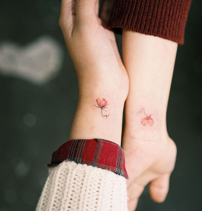 Matching flower tattoos on two wrists, symbolizing BFF friendship.