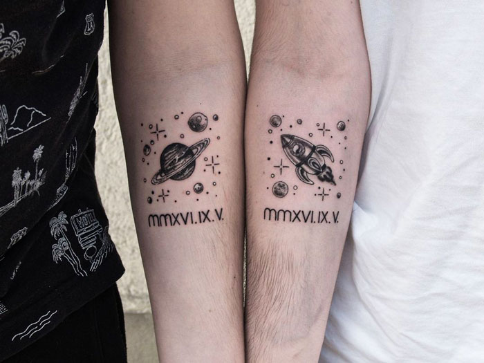 Matching best friend tattoos featuring a planet and rocket design on forearms, symbolizing lasting friendship.