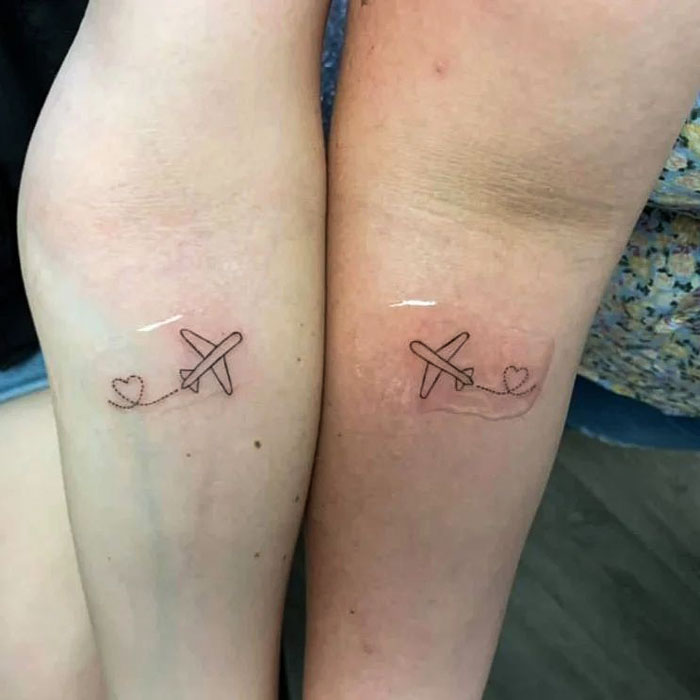 Matching best friend tattoos of airplanes with heart trails on forearms.