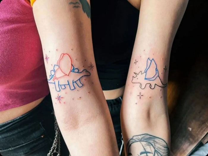 Two arms with matching dinosaur best friend tattoos, symbolizing their awesome friendship.