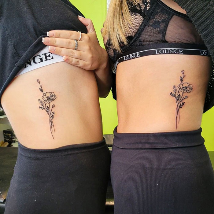 Two friends displaying matching flower tattoos on their sides to commemorate friendship.