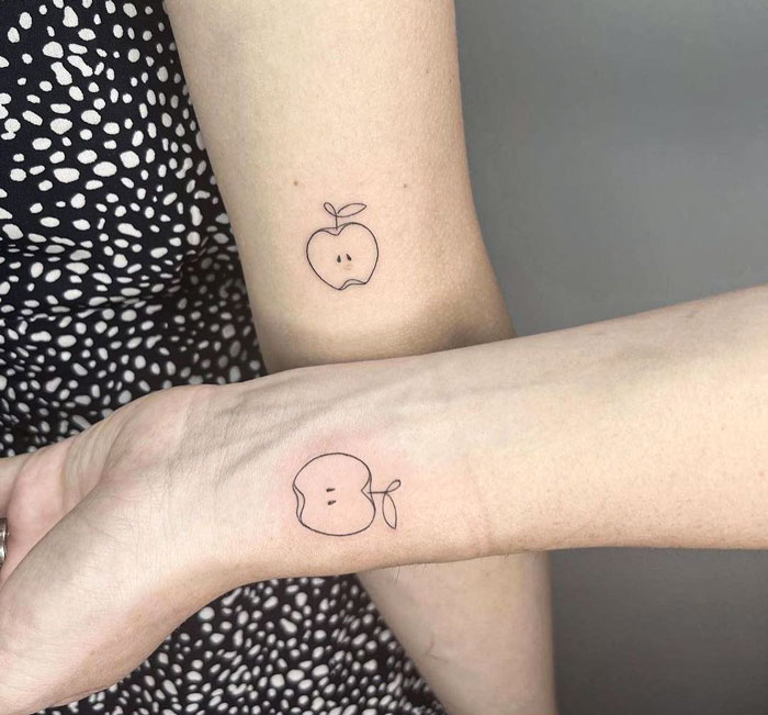 Matching minimalist apple friend tattoos on forearms symbolize friendship and connection.