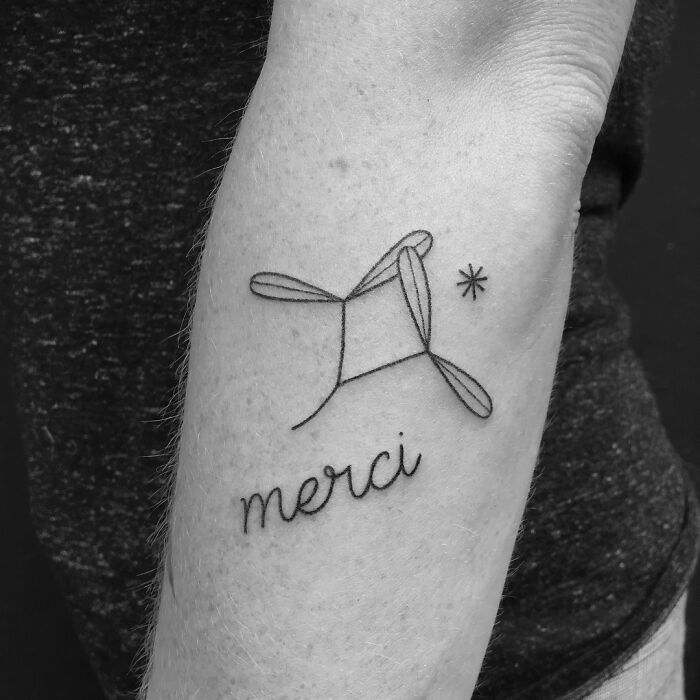 Minimalist word tattoo "merci" with geometric design on forearm, showcasing unique tattoo art.