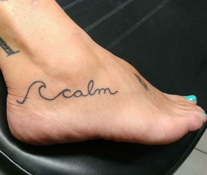 Creative word tattoo on foot, reading "calm" with a wave design, highlighting tattoo ink inspiration.