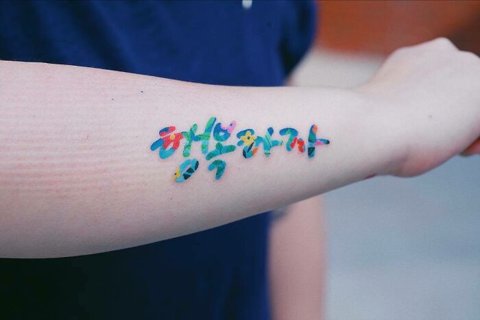 Colorful word tattoo on a forearm with Korean characters.