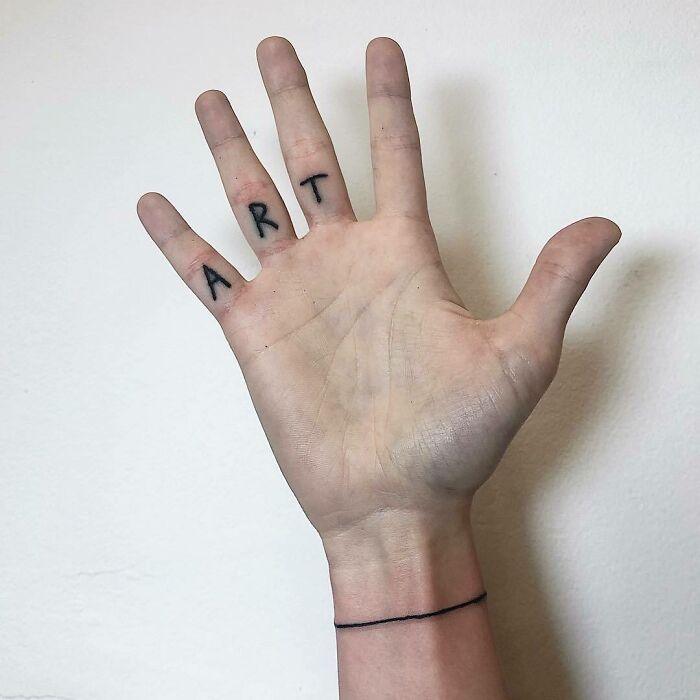 Hand with the word "ART" tattooed on fingers, featuring minimalist tattoo ideas for new ink inspiration.